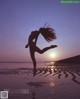 A woman jumping in the air on a beach at sunset.