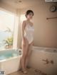 A woman in a white bathing suit standing next to a bathtub.