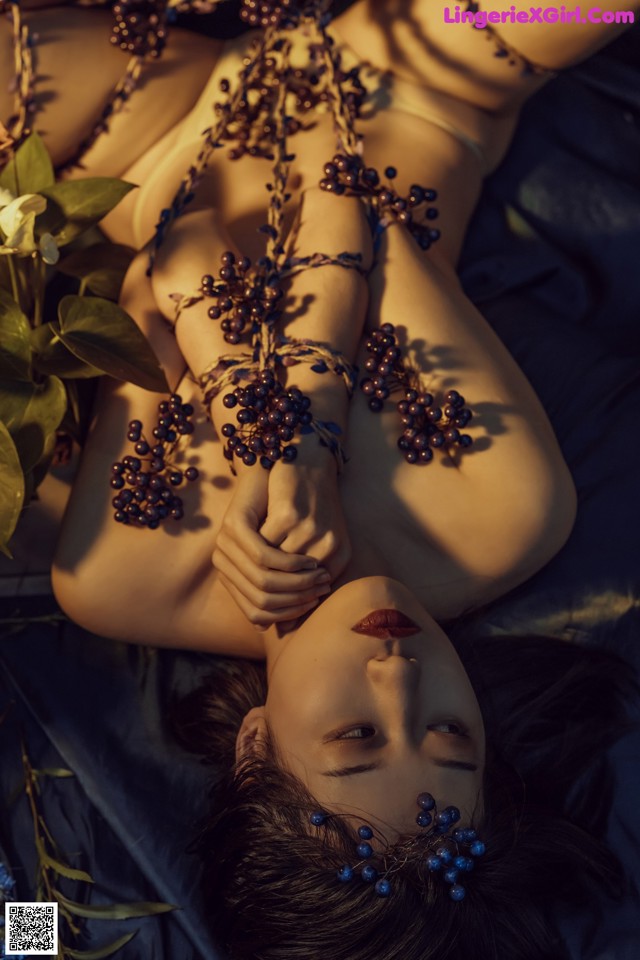 A woman laying on a bed covered in blueberries.