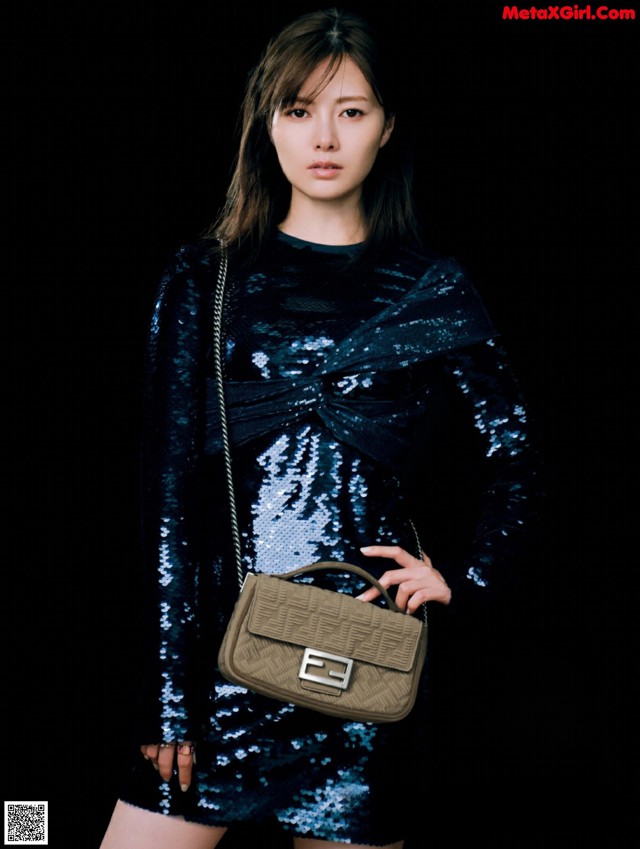 A woman in a blue dress holding a brown bag.