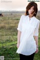 A woman standing in a field with a horse in the background.