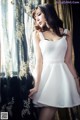 A woman in a white dress standing by a window.