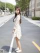 A woman in a white dress is standing on the street.