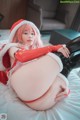 A woman in a santa claus outfit is sitting on a bed.