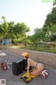 A woman in a yellow helmet is sitting on the ground next to a suitcase.