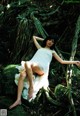 A woman in a white dress sitting on a rock in the woods.