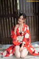 A woman in a red kimono sitting on the ground.